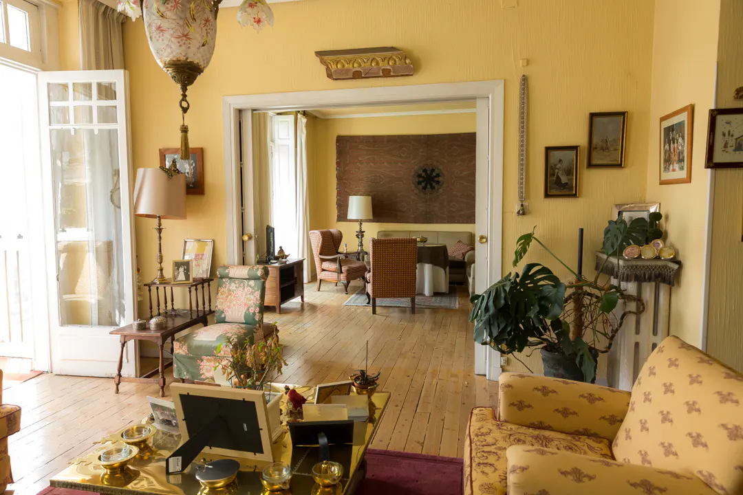 A yellow living room with floral furniture, a gold coffee table, and framed pictures on the wall.