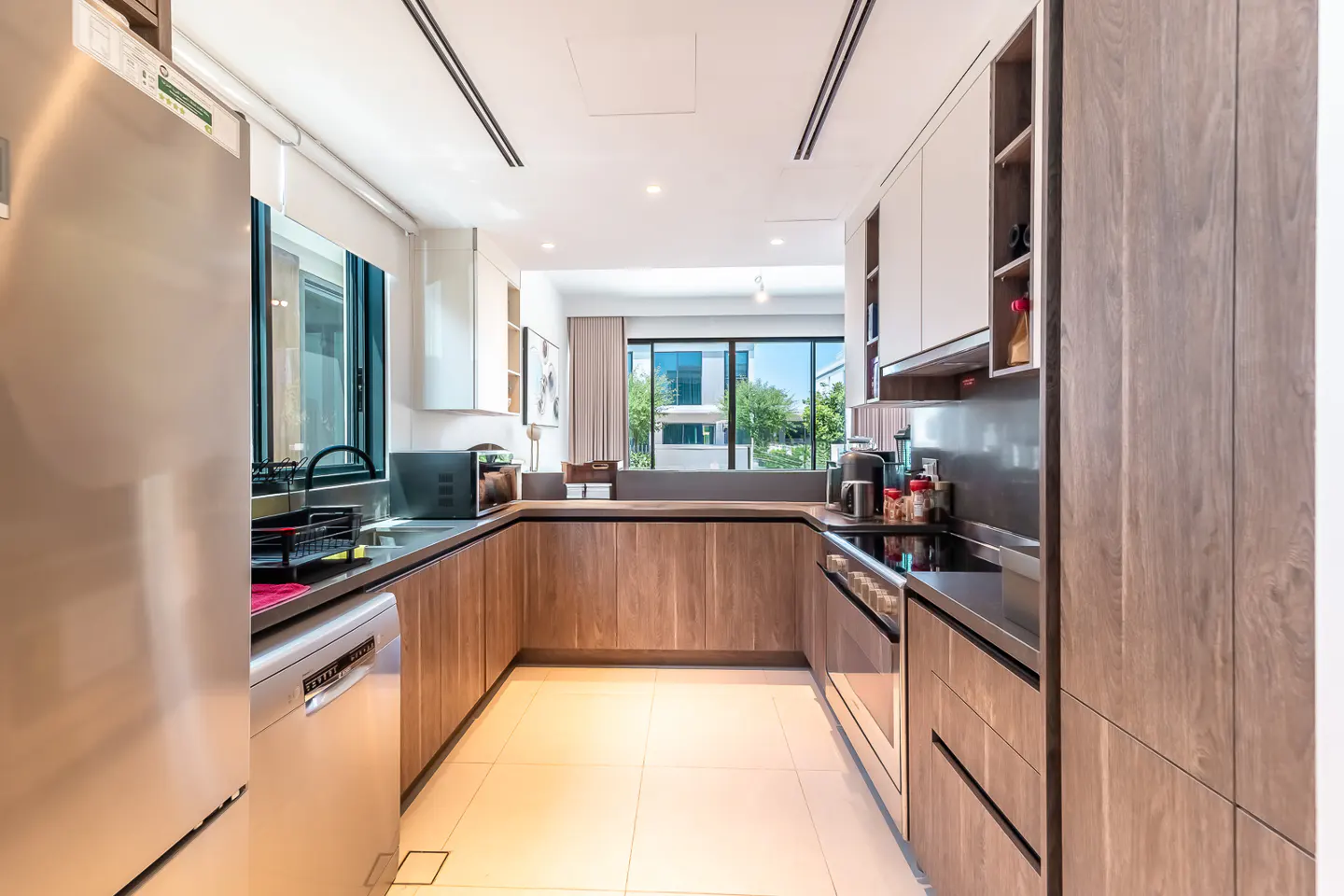 Modern U-shaped kitchen with wood-grain cabinets, stainless steel appliances, and large windows overlooking greenery.