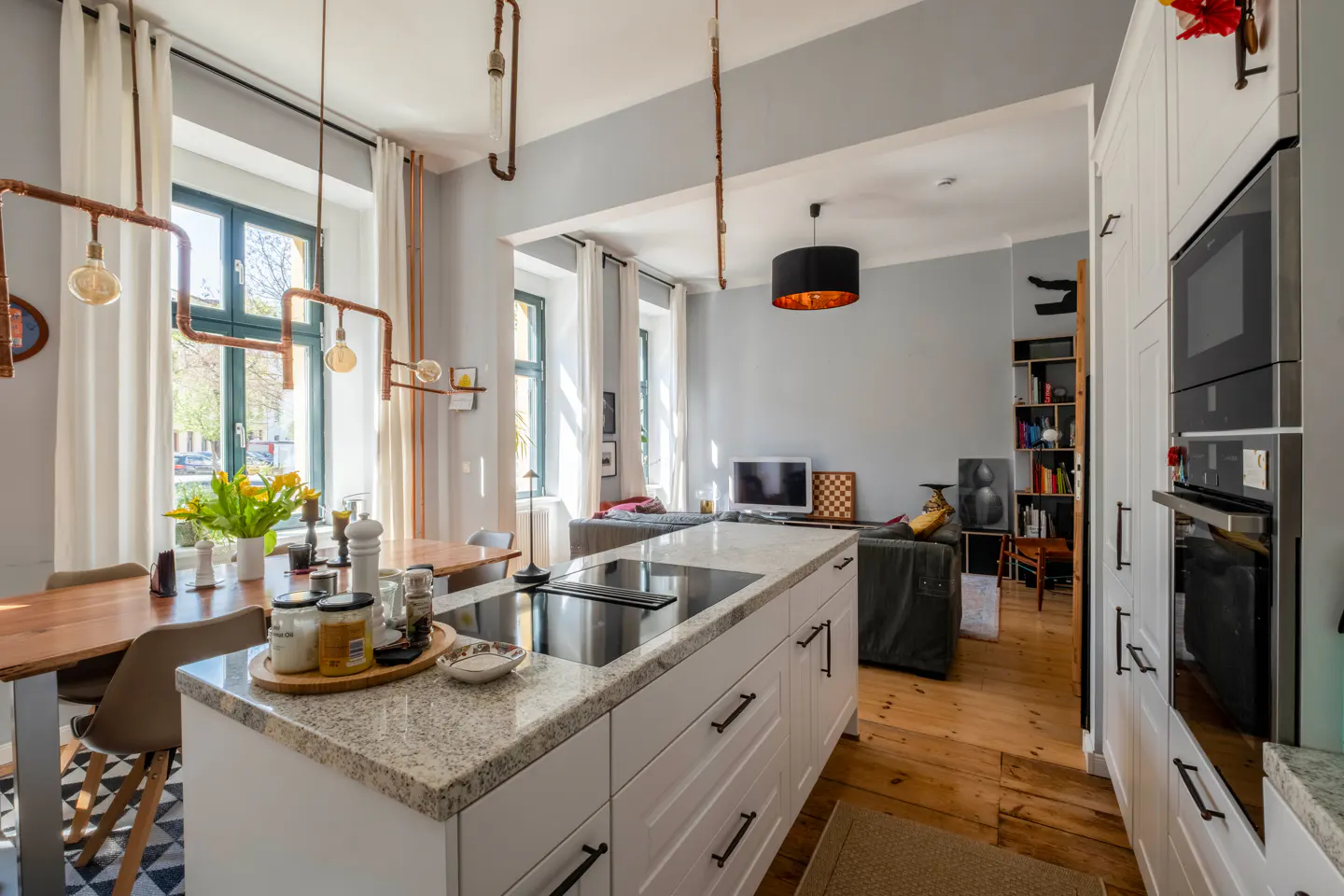 Open concept kitchen and living room with white cabinets, wood floors, and copper pipe lighting fixtures.