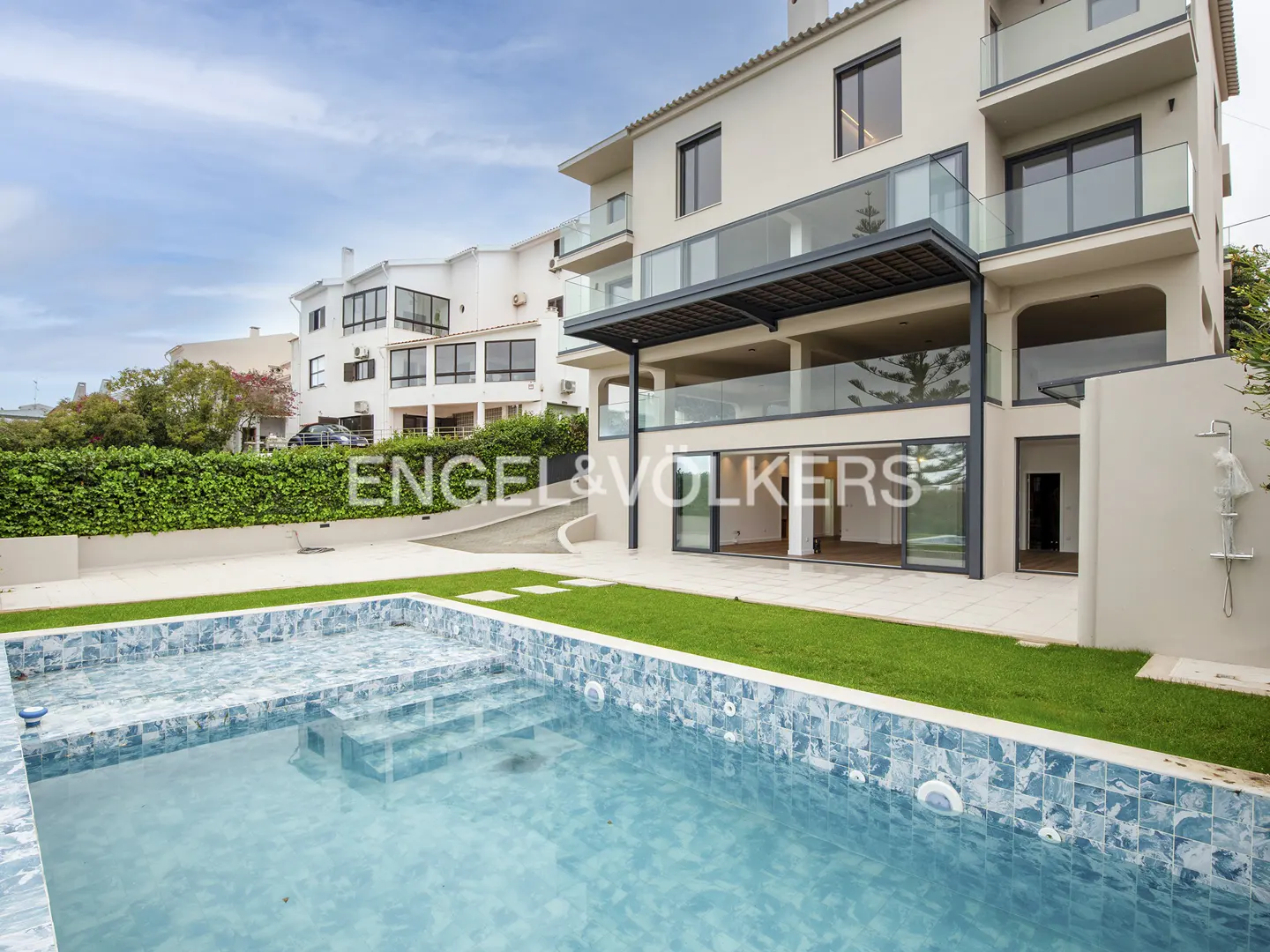 Exterior view of a modern, multi-story home with a blue-tiled pool in the foreground and a green hedge in the background.