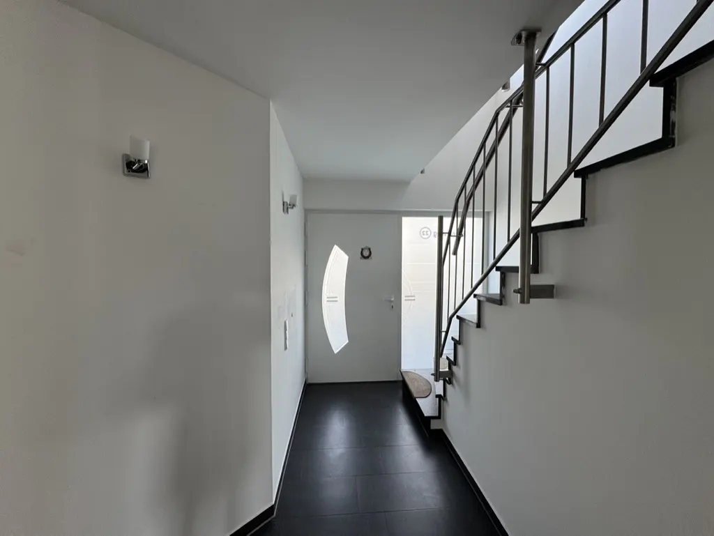 Hallway with black tile floor, white walls, and a staircase with metal railings. A white door with a curved window is visible.