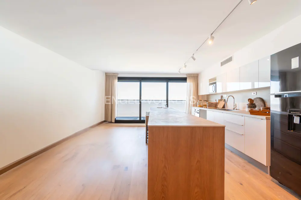 Bright, modern kitchen with wood floors, white cabinets, and a wood island. A black refrigerator is on the right, and a balcony is in the background.