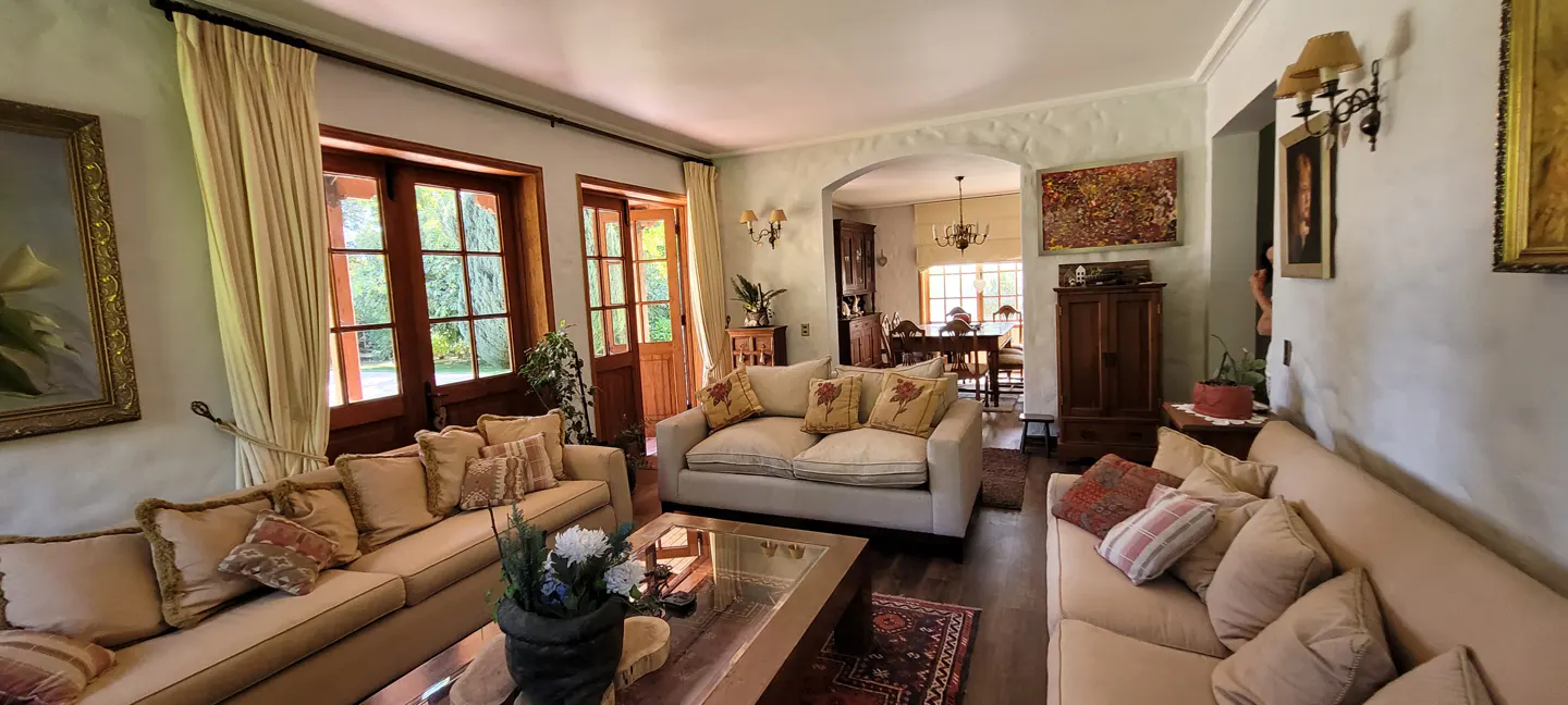 Living room with beige sofas, wooden doors to the outside, and an arched doorway leading to a dining room.