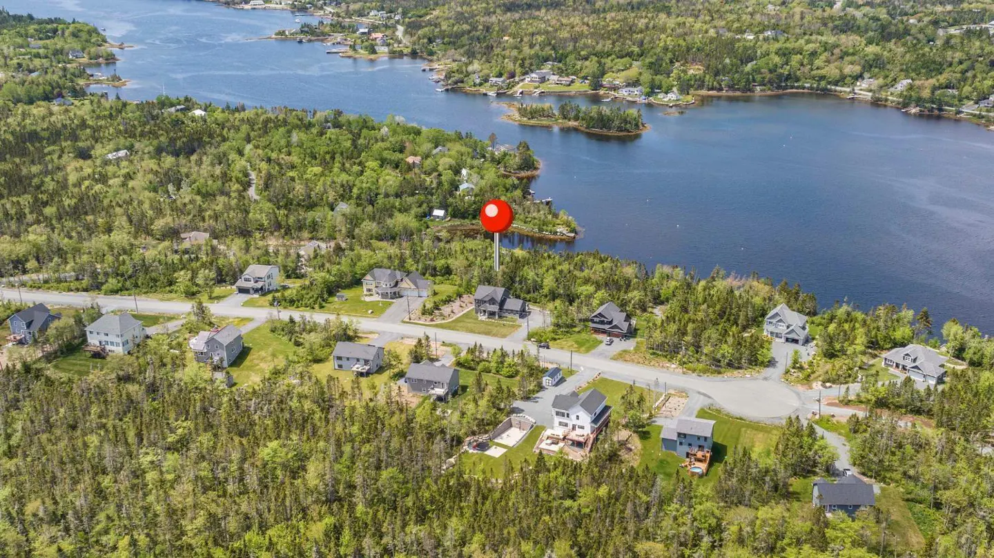 Aerial view of houses near a lake, surrounded by green trees. A red pin marks a property.