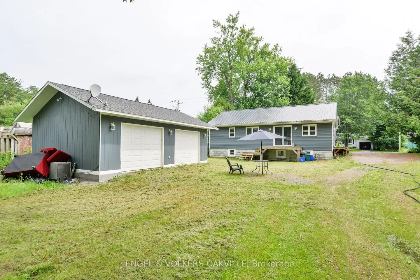 Exterior view of a gray house with a detached garage, green lawn, and patio set with umbrella.