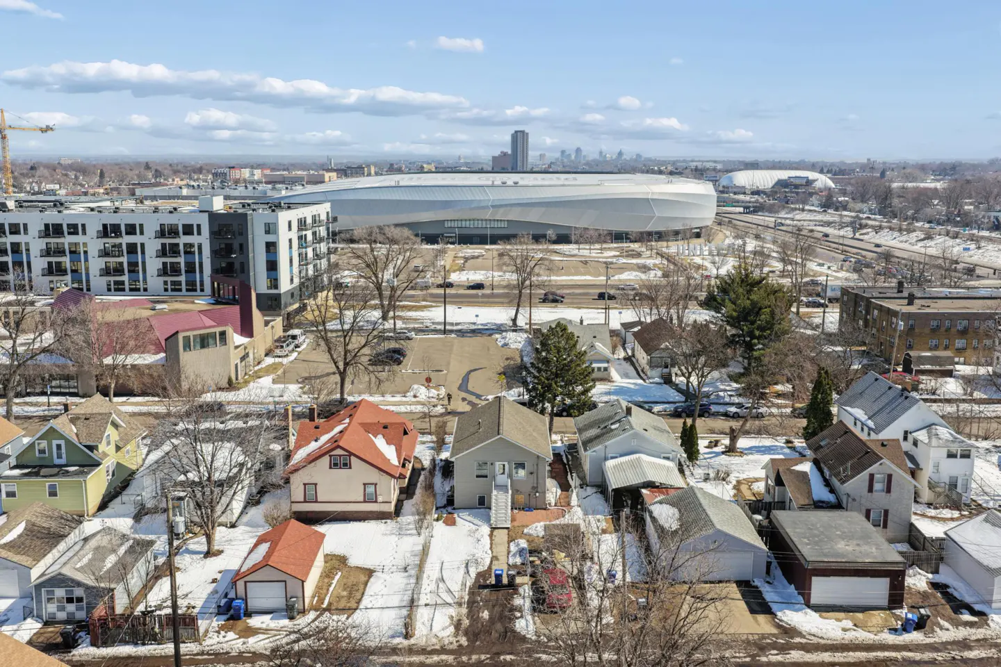 Aerial view of a neighborhood with houses, a stadium, and a city skyline in the background on a sunny day.