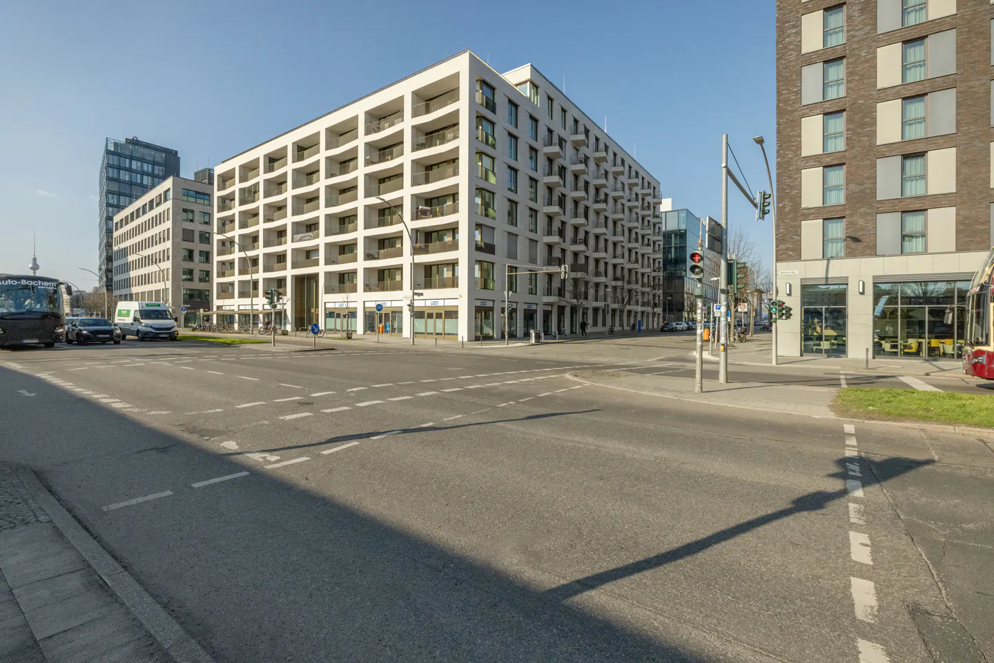Cityscape view of modern apartment buildings with balconies, seen from a street intersection on a sunny day.