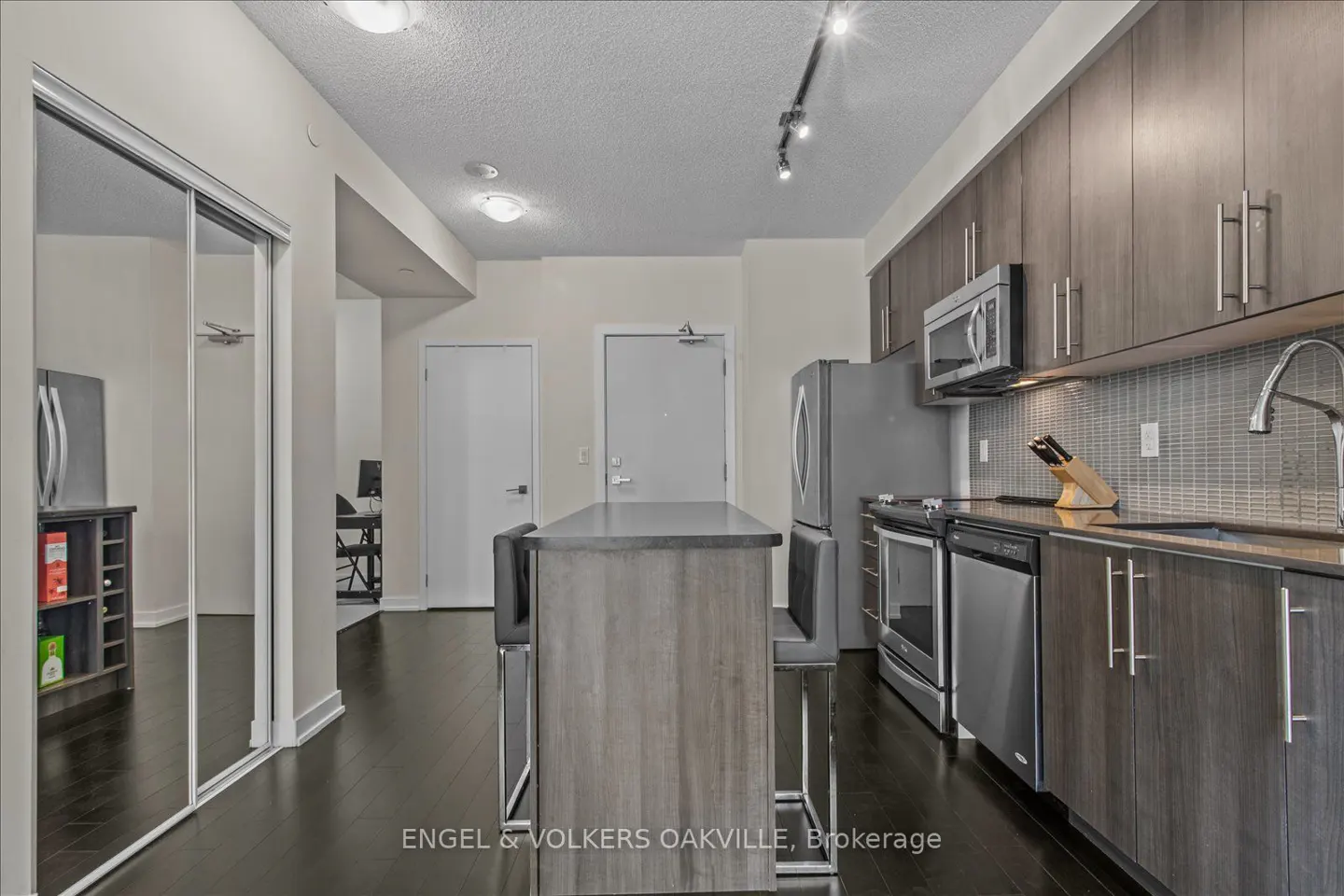 A modern kitchen with dark wood floors, gray cabinets, stainless steel appliances, and a kitchen island with seating.