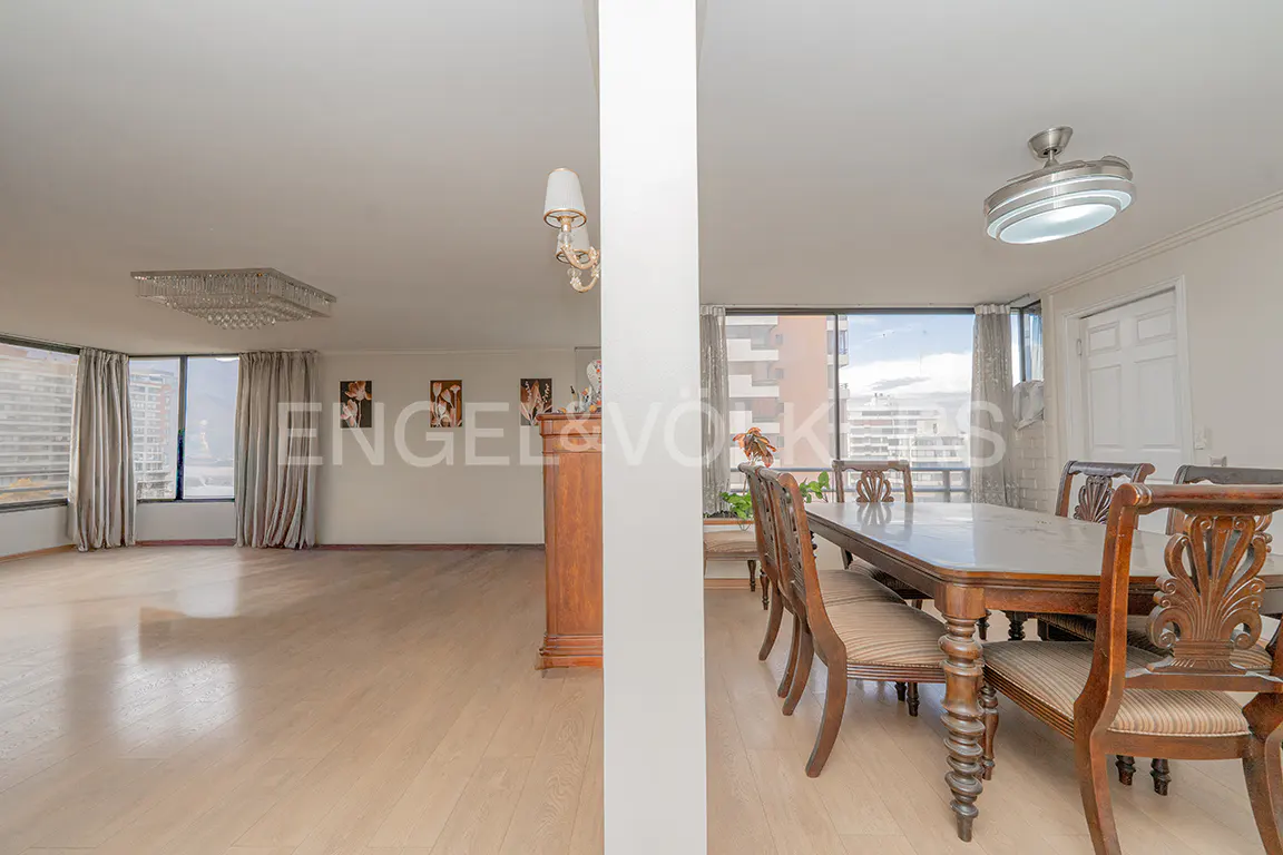 Open-concept living and dining room with light wood floors and large windows. A white column divides the space. Dining table with chairs is on the right.