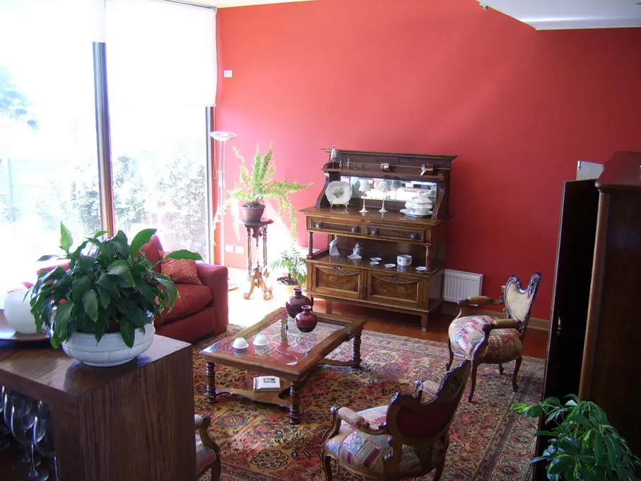 Living room with red wall, large window, patterned rug, and antique furniture, including a wooden hutch and chairs.