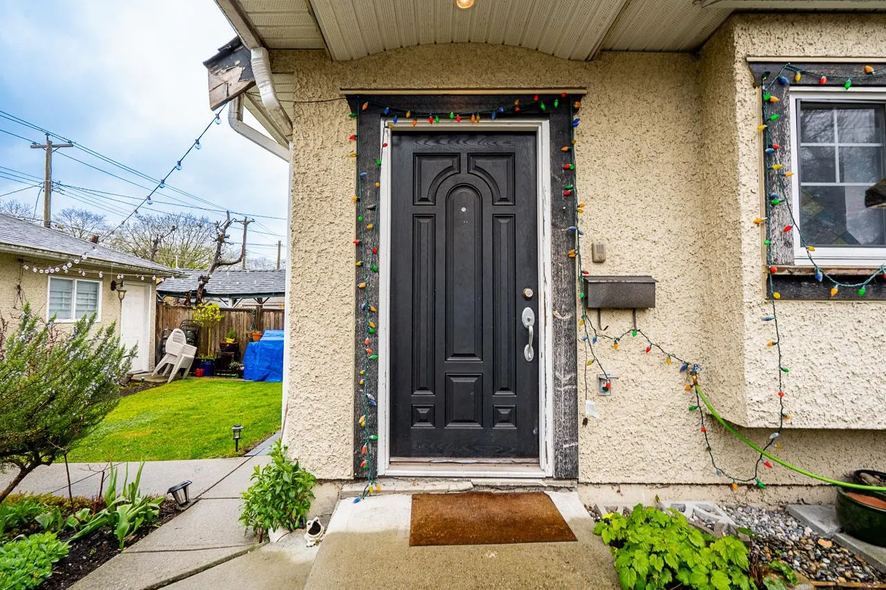 Front door of a beige house, framed with colorful Christmas lights. A window is to the right of the door.