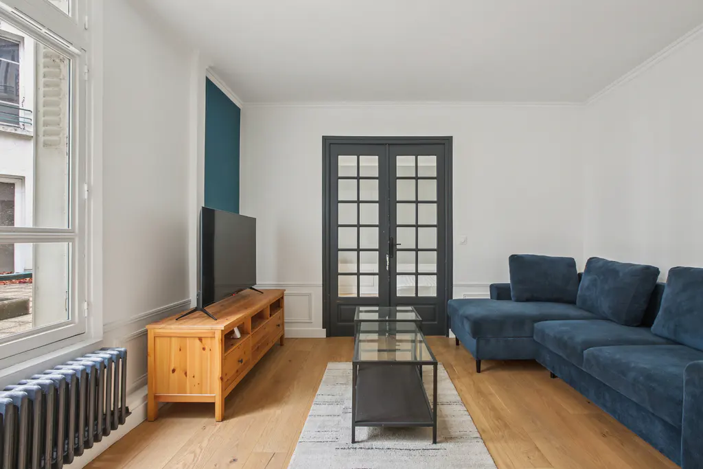 Living room with a blue sofa, wood floors, a TV on a wood stand, and a black framed glass door.