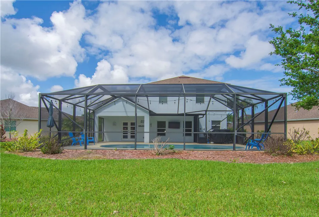 Backyard view of a white house with a screened-in pool enclosure and blue chairs.