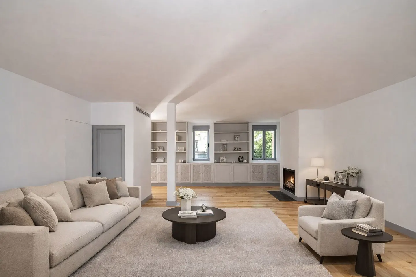 Bright living room with beige sofa, armchair, and rug. Built-in bookshelves and a fireplace add character.