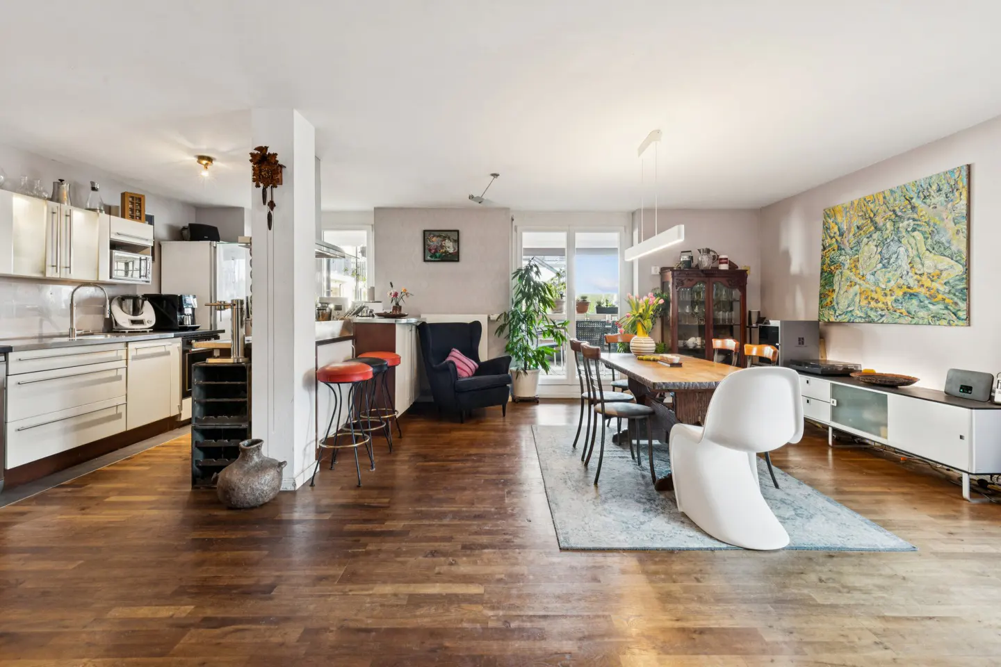 Open-concept living space with a kitchen, dining area, and lounge. Hardwood floors, white cabinets, and a large abstract painting are visible.