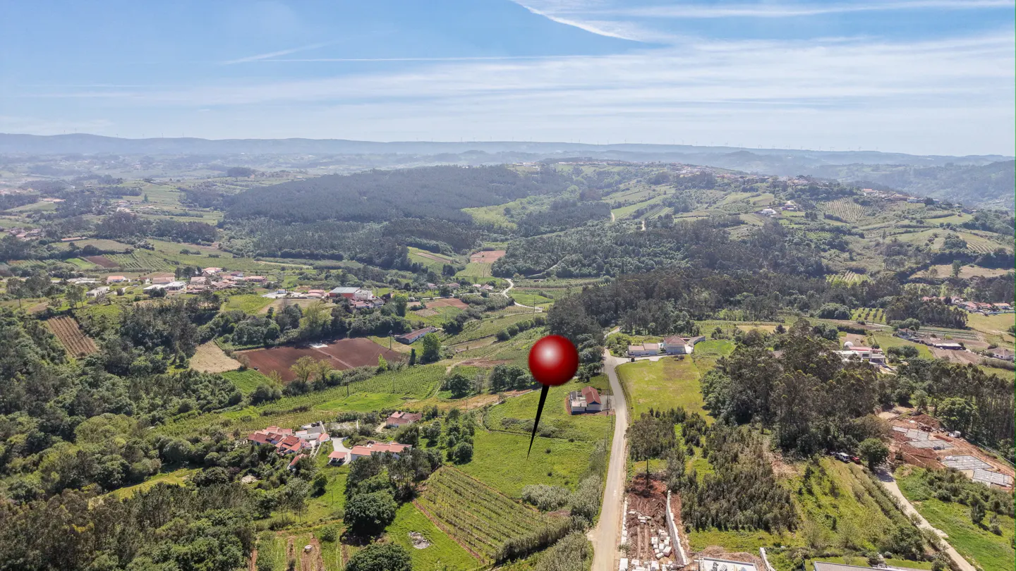 Aerial view of a rural landscape with a red pin marking a property. Rolling hills, trees, and scattered houses under a blue sky.