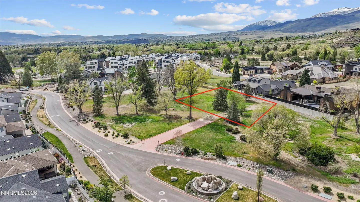 Aerial view of a vacant lot outlined in red, surrounded by houses, trees, and mountains in the background.