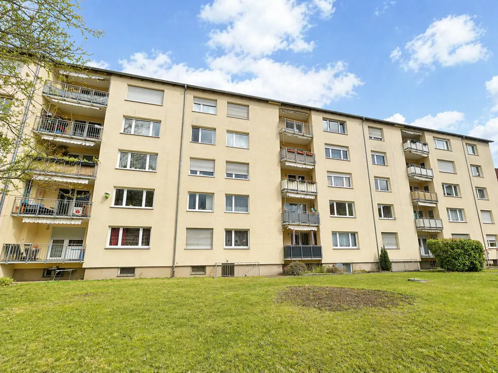 A low-angle shot of a yellow apartment building with balconies and a green lawn in front.