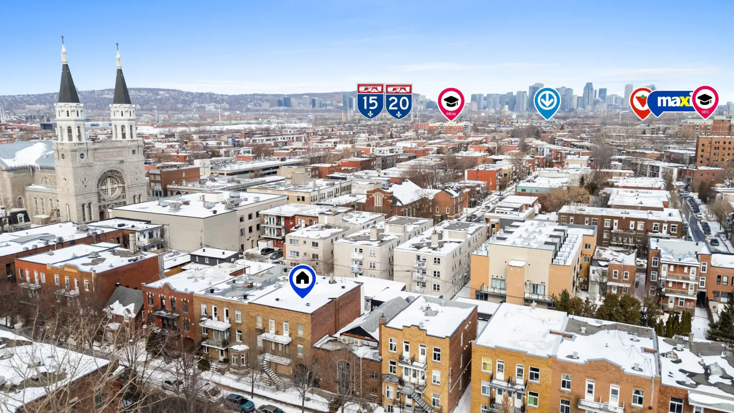 Aerial view of a city neighborhood in winter, with a church and city skyline in the background.