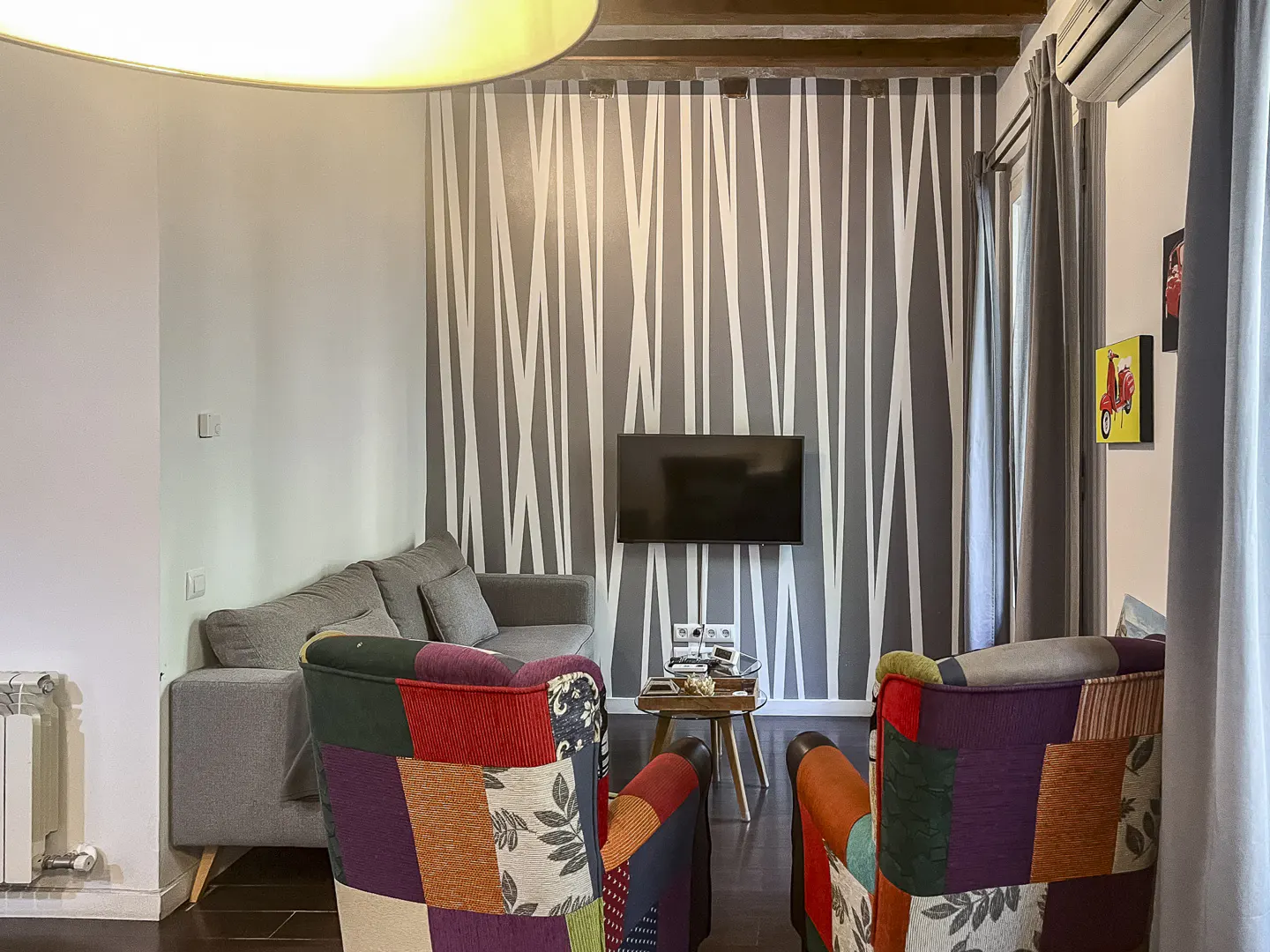 Living room with two colorful patchwork armchairs, a grey sofa, and a wall with white vertical stripes and a mounted TV.