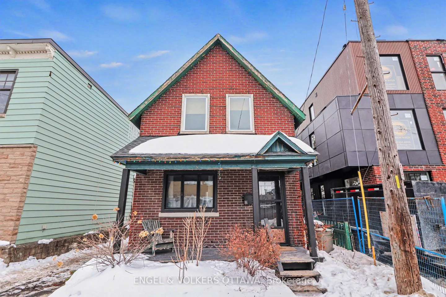 A two-story red brick house with a green roof and black trim, snow on the ground, and a blue sky.