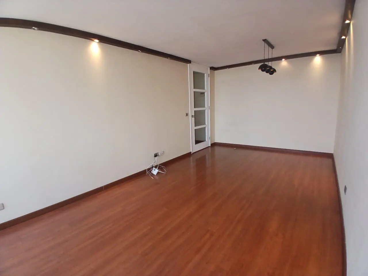 Empty room with light-colored walls, polished wood floors, recessed ceiling lighting, and a white glass-paneled door.