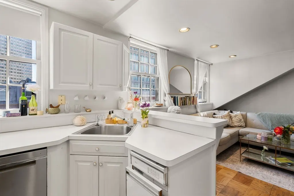 Bright, open-concept apartment with white kitchen cabinets, stainless steel appliances, and a living area with a beige sofa and glass coffee table.