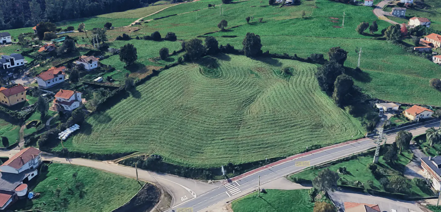 Aerial view of a large, green, grassy field bordered by houses and roads in a rural area.