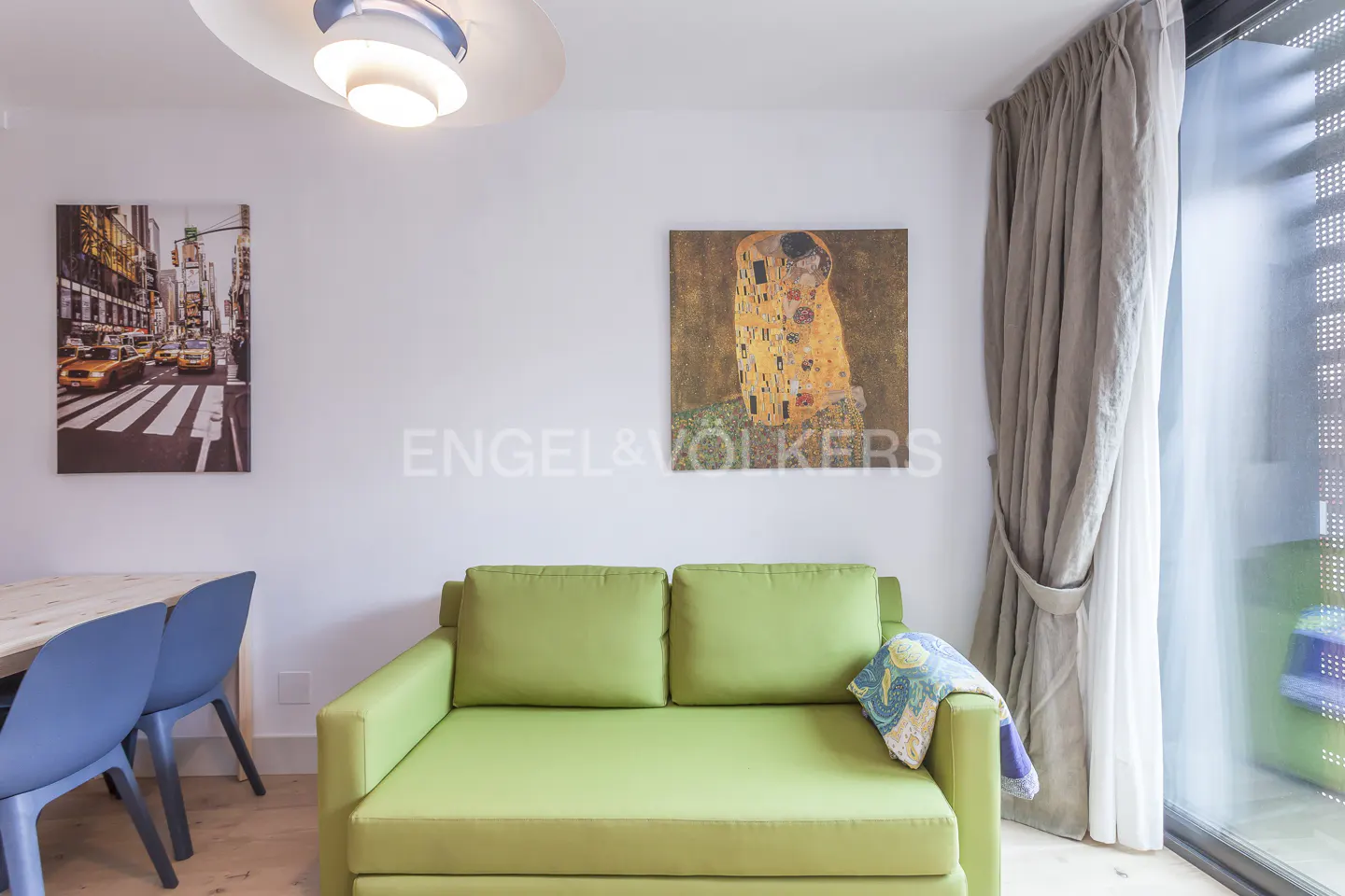 Living room with a green sofa, blue chairs, and artwork of New York and "The Kiss" by Klimt.