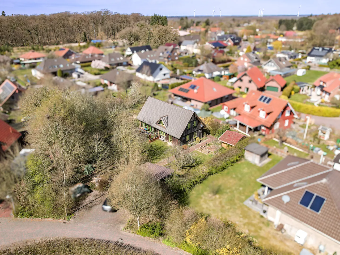 Aerial view of a brown house with a gray roof, surrounded by trees and other houses in a rural setting.