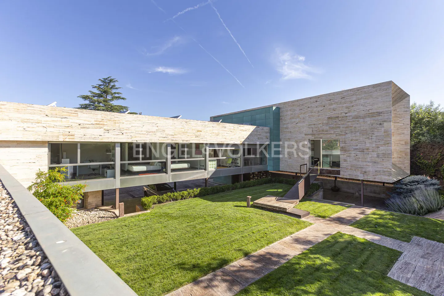 Exterior view of a modern, two-story home with a stone facade, large windows, and a green lawn.