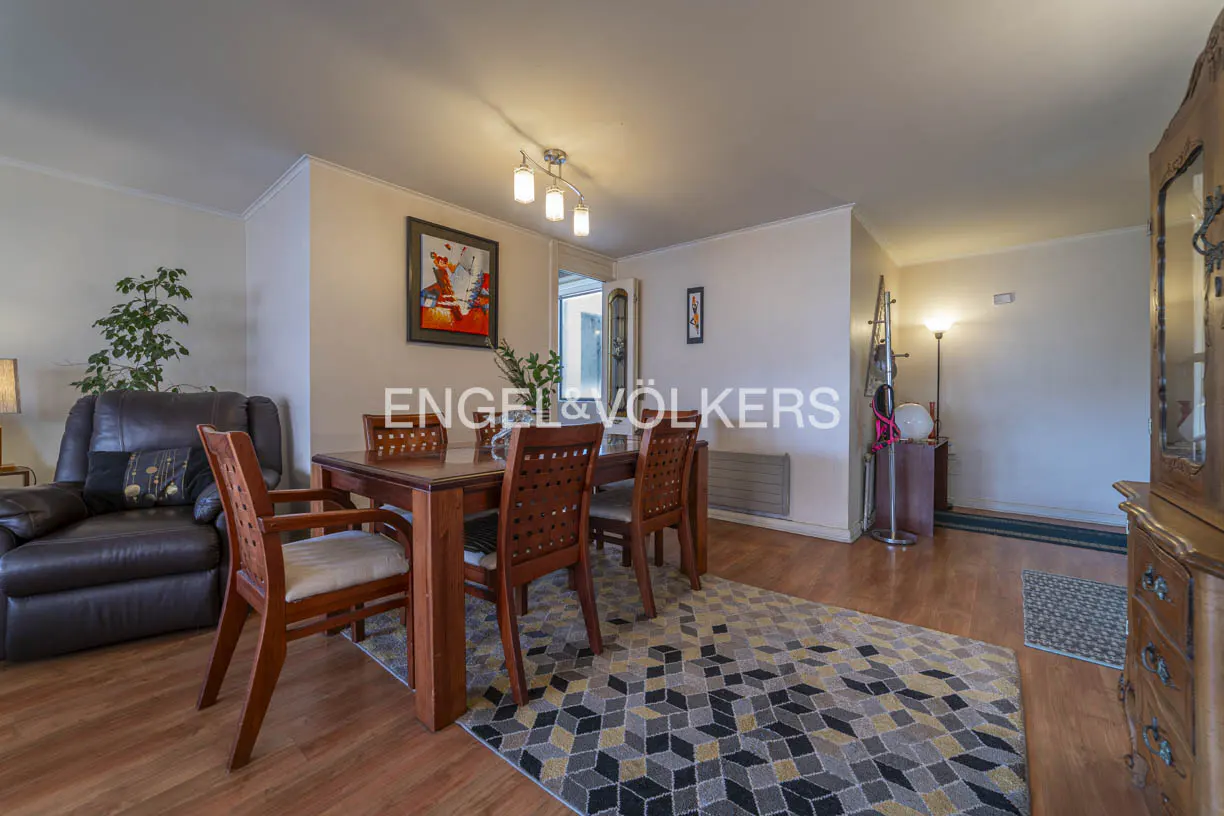 Living room with a wooden dining table, chairs, and a brown leather recliner. A patterned rug covers the wood floor.