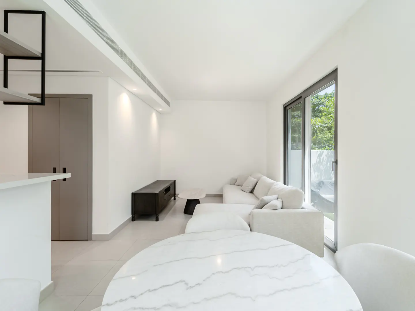 Bright, modern living room with white walls, a marble table, and a white sectional sofa near a sliding glass door.
