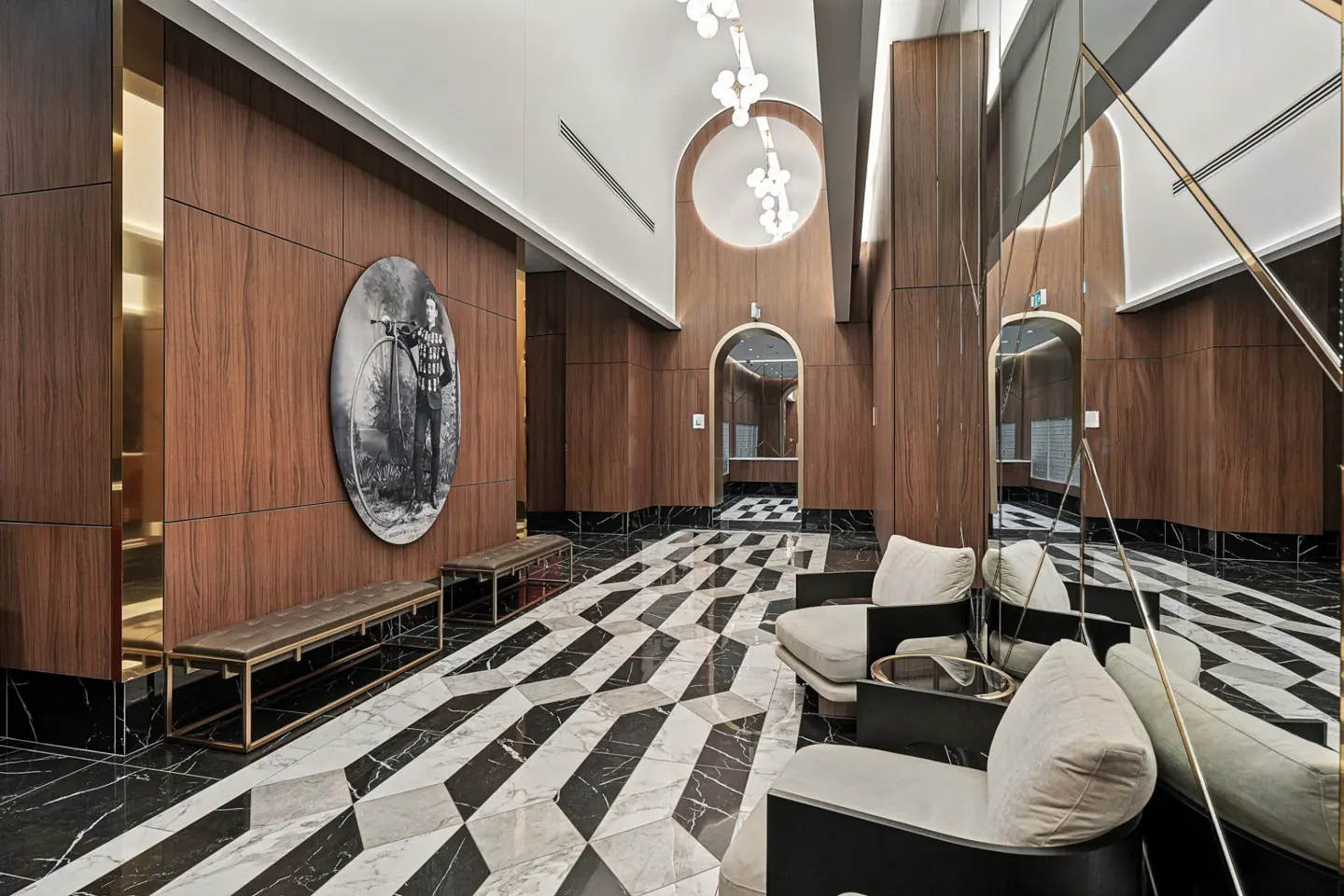 A modern lobby with wood paneled walls, black and white marble floors, and seating. A vintage bicycle print hangs on the wall.