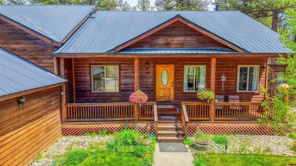 A cozy, brown, wood cabin with a metal roof and a porch with flower baskets.