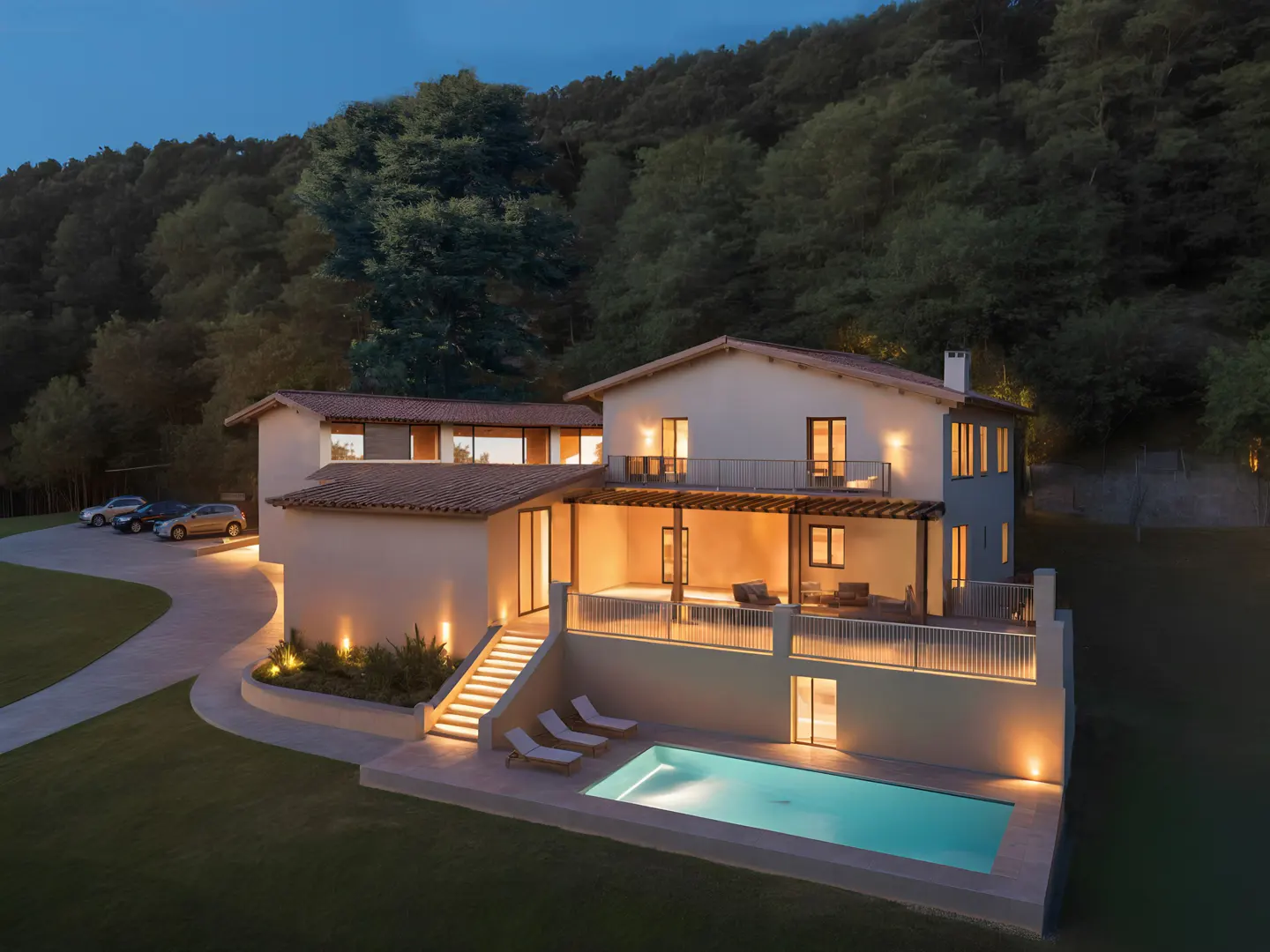 Two-story villa at dusk with a lit pool, patio, and driveway, set against a backdrop of dense forest.
