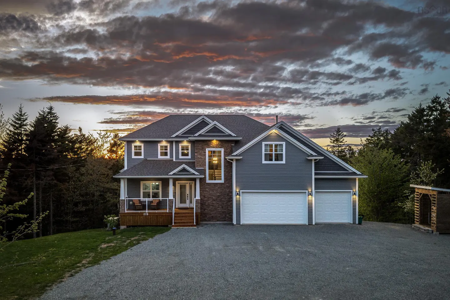 Two-story gray house with white trim and a two-car garage at dusk. Trees and a colorful sky are in the background.