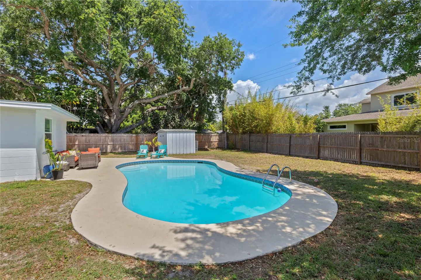 Backyard with a kidney-shaped pool filled with blue water, surrounded by a concrete patio and green grass. A wooden fence encloses the yard.