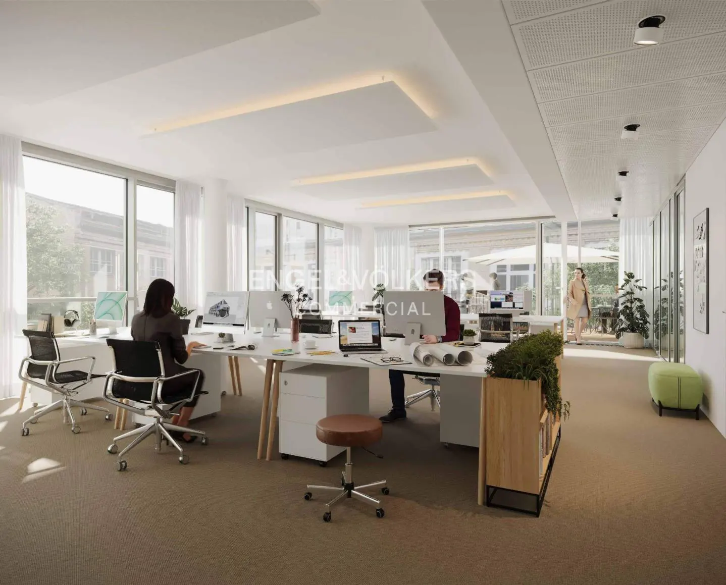Bright, modern office space with white desks, computers, and large windows. People are working at desks. A woman walks in the background.