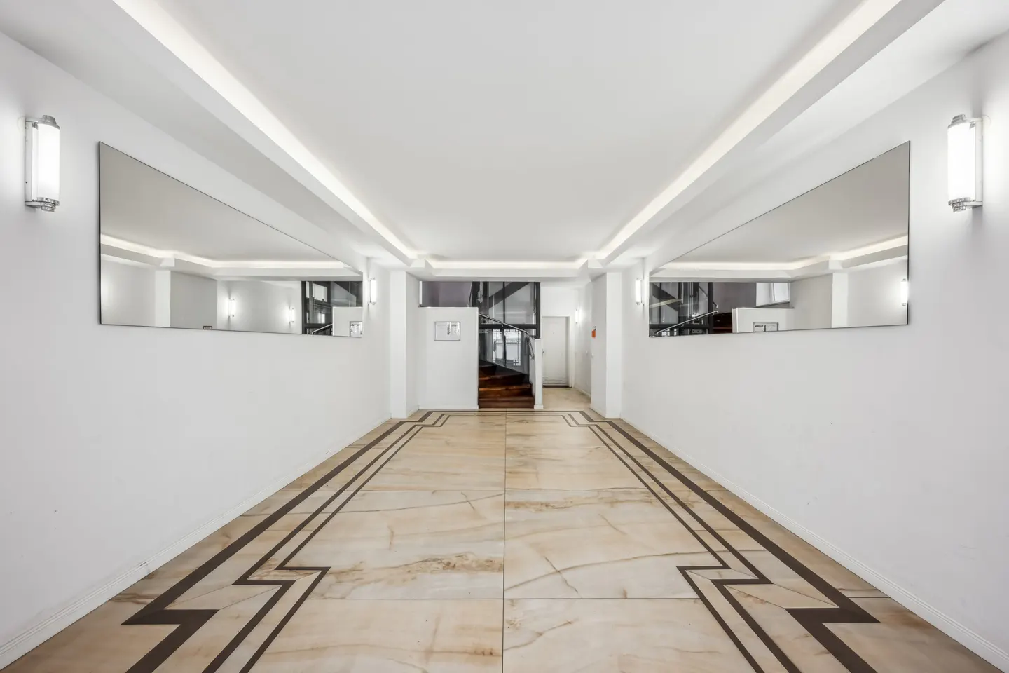 Hallway with marble floors, white walls, and large mirrors. A staircase is visible in the background.