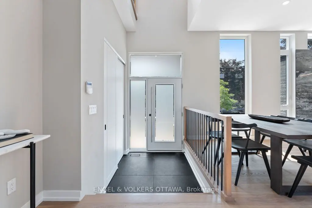 A bright foyer with a white door, frosted glass, and black tile floor. A dining table and chairs are visible through a railing.
