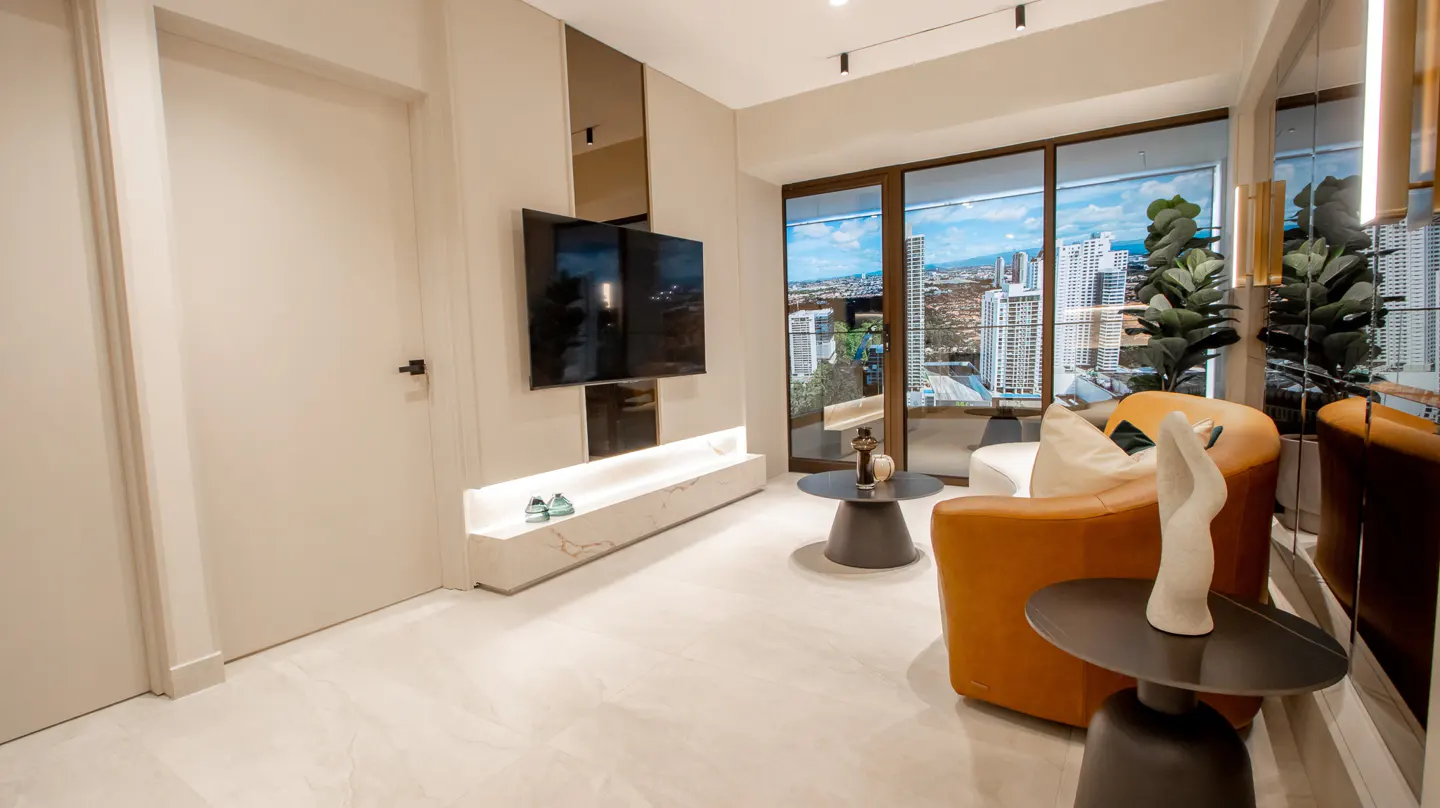 Modern living room with a TV, brown leather chairs, and a city view through large windows.