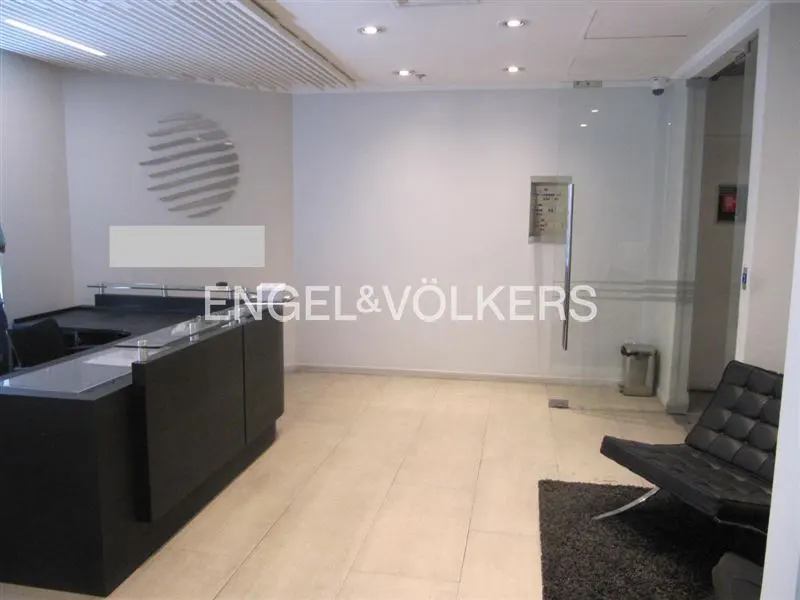 Engel & Völkers office reception area with a black desk, logo on the wall, and a black chair on a gray rug.