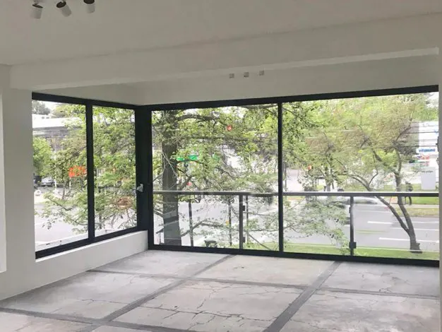 Empty room with large windows overlooking a street with trees. The floor is concrete and the walls are white.