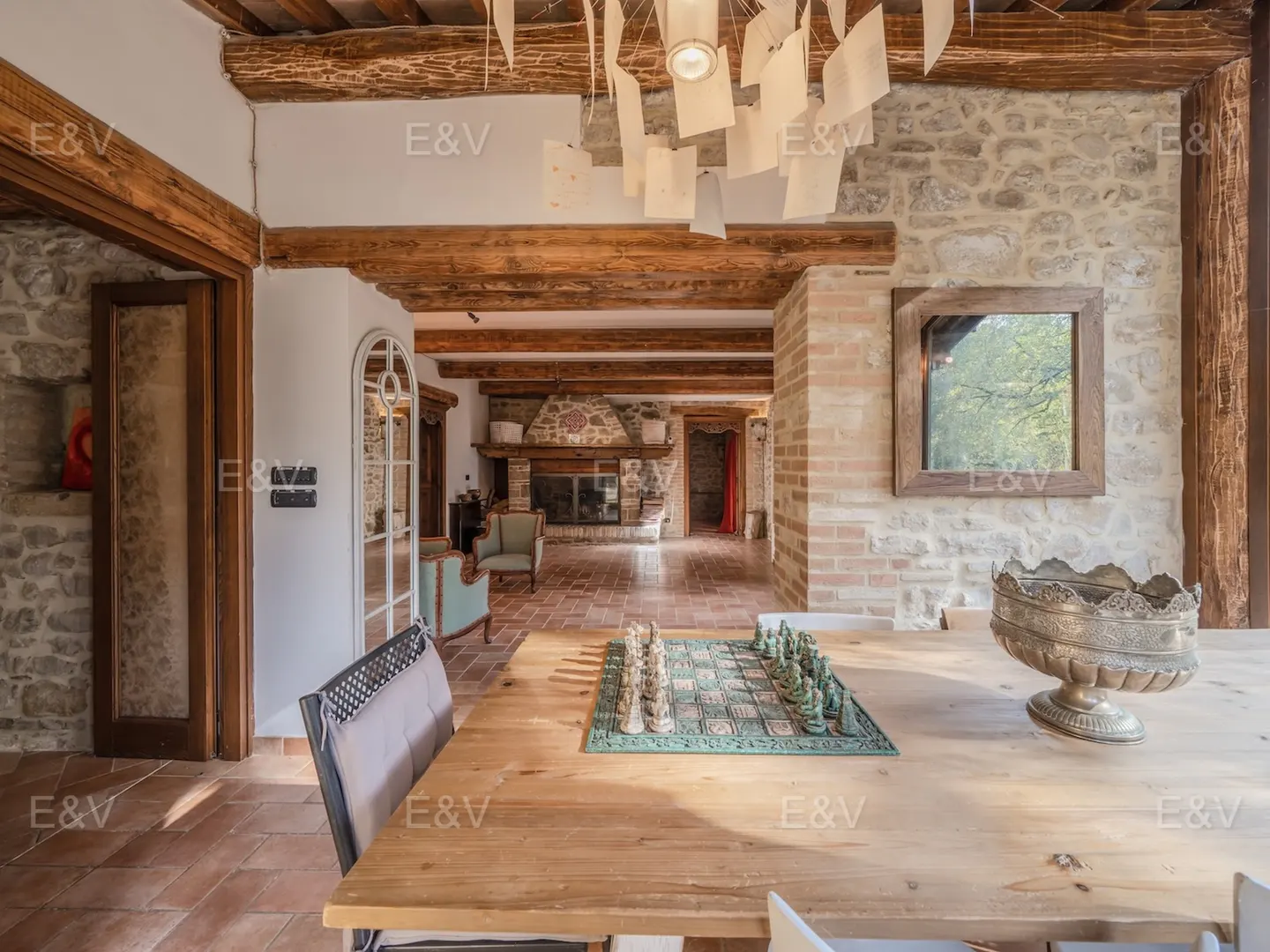 Interior view of a rustic dining room with stone walls, wooden beams, and a chess set on a light wood table.