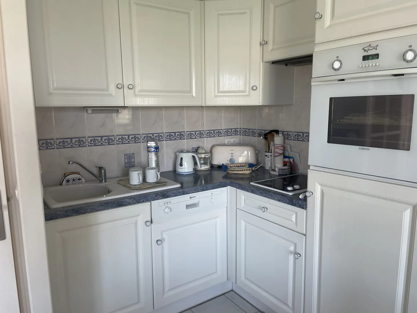 A bright kitchen with white cabinets, blue-trimmed backsplash, sink, and oven.