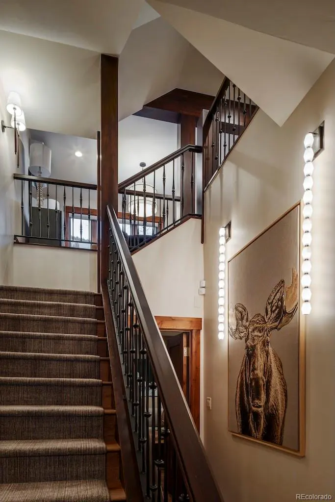 Interior view of a staircase with brown carpet, dark wood railings, and a moose painting on the wall.