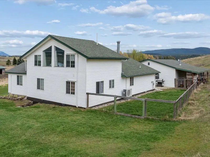 Exterior view of a two-story white house with a green roof, surrounded by a green lawn and a wooden fence.