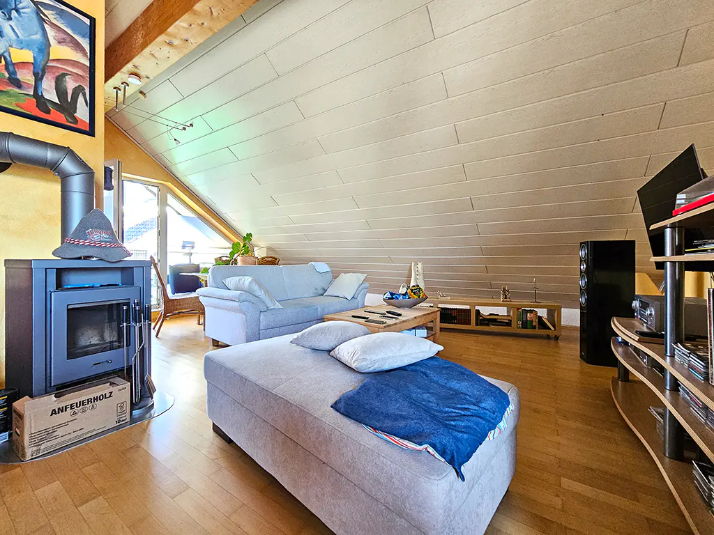 Attic living room with wood floors, a gray sofa, ottoman with blue blanket, fireplace, and a sloped ceiling.