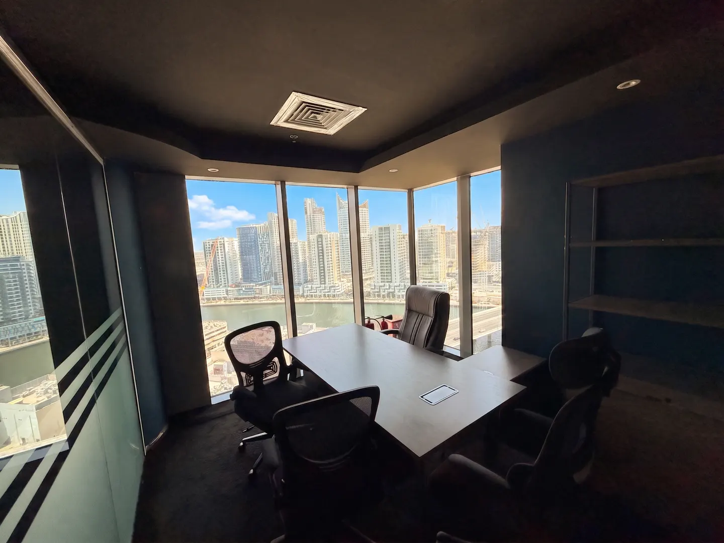 A modern office with a large window overlooking a city skyline, featuring a conference table and chairs.